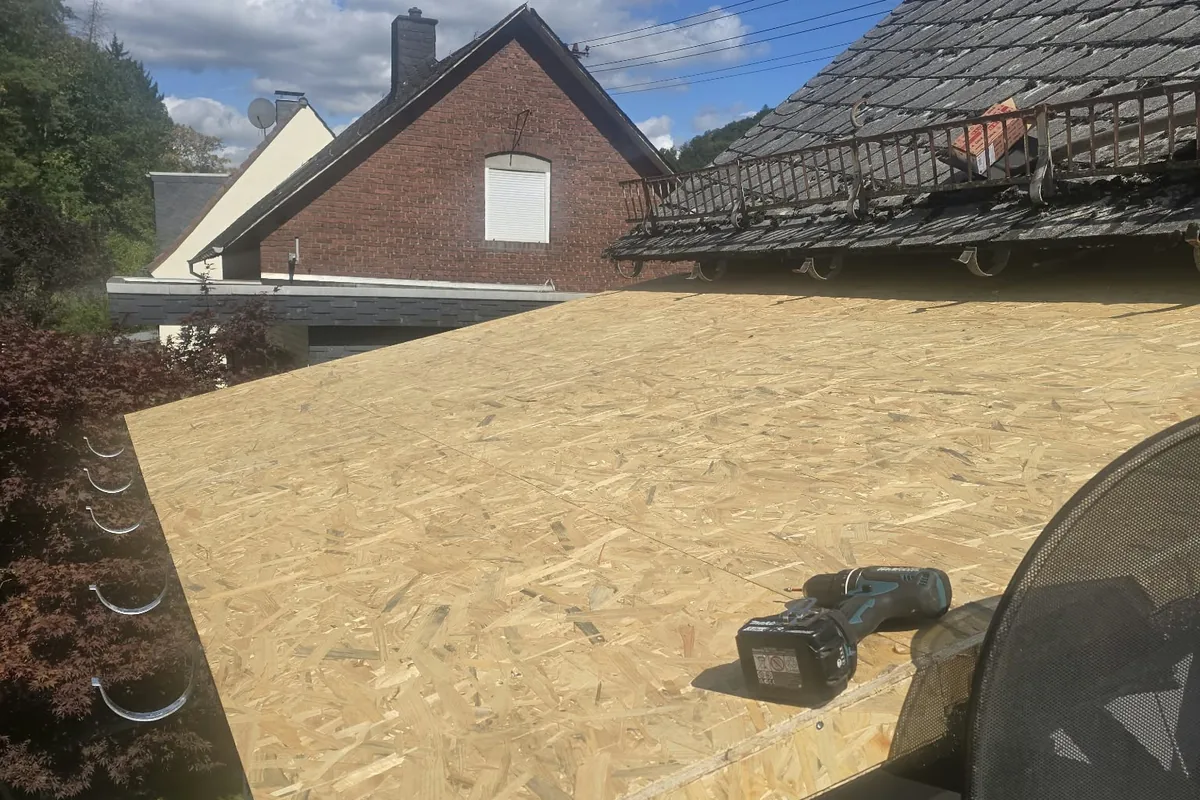 Flachdach mit neu verlegter Unterkonstruktion aus Holzplatten, dahinter ein Wohnhaus