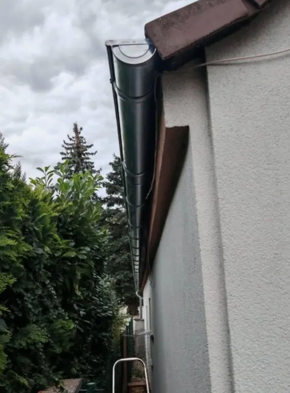 Dunkles Fallrohr an einer hellen Hauswand, dahinter blauer Himmel