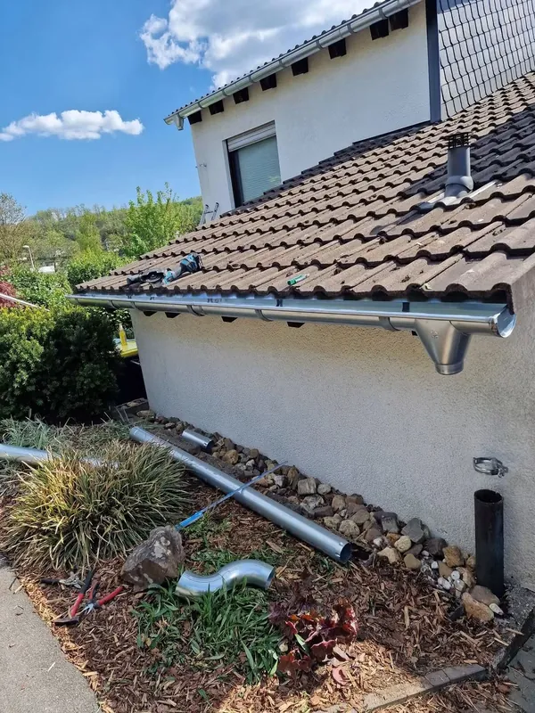 Haus mit neuer Dachrinne, davor liegen die Fallrohrteile im Beet